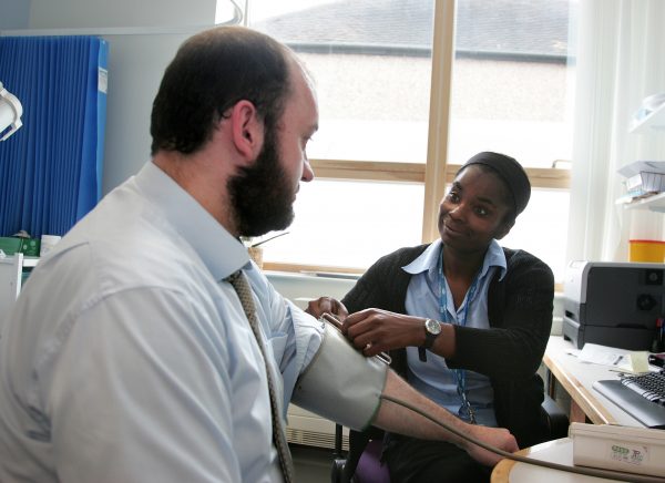 Unique ID: LL4A9773

Caption: Polylinic or GP surgery appointment. A visit to the healthcare assistant or practice nurse. A woman in nursing uniform. Talking to a man with a beard. Wearing a blood pressure cuff. Monitoring a patient's blood pressure. Routine check up. Assessment.

Restrictions: NHS Photo Library - for use in NHS, local authority Social Care services and Department of Health material only

Copyright: ©Crown Copyright