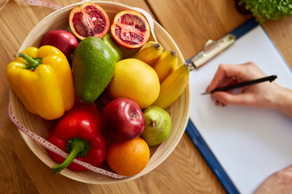 Dietitian woman writing a diet plan, with healthy vegetables and fruits